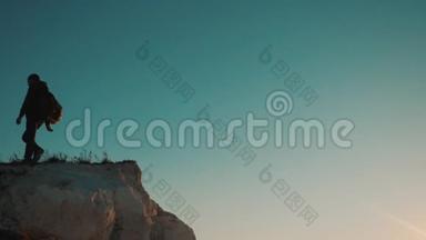 一位男子游客在日落时爬上山顶冒险生活方式冒险的剪影。 剪影